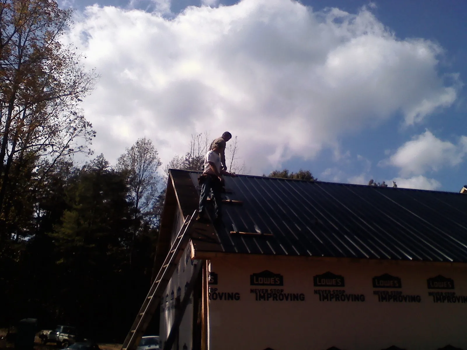 Roofer fastening dark metal panels high against a cloudy sky, from a Roof Inspection job in Brunswick